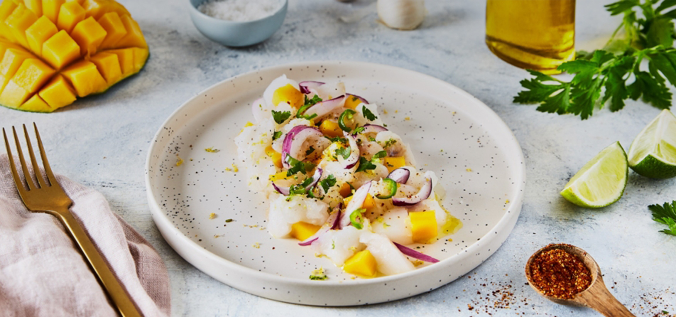Ceviche de poisson blanc avec mangue, oignon rouge, piment et coriandre, accompagné de citrons verts.
