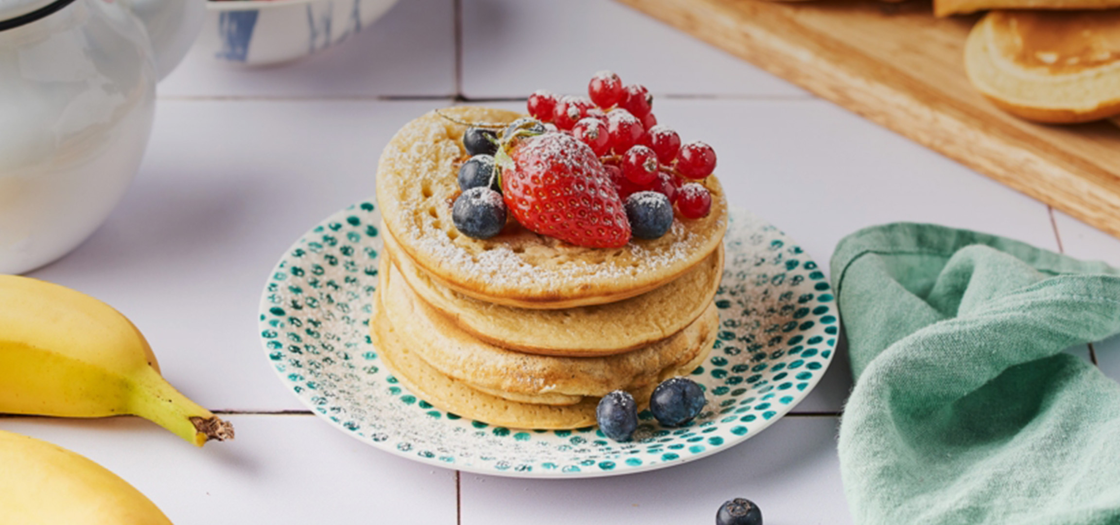 Pile de pancakes avec des fruits rouges, des myrtilles et du sucre glace sur une assiette.