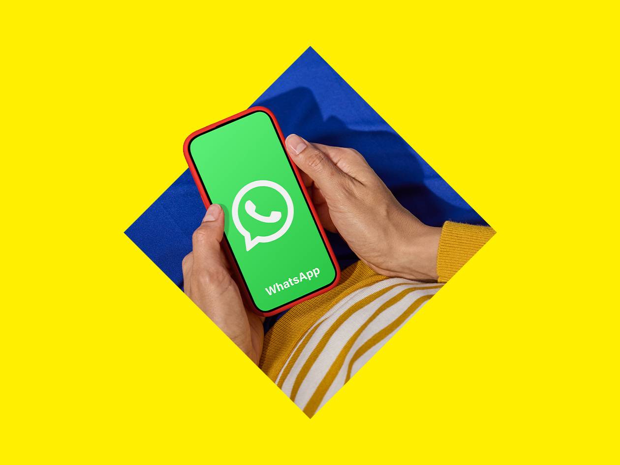 Mains tenant un smartphone avec une application de messagerie sur un fond jaune et bleu.