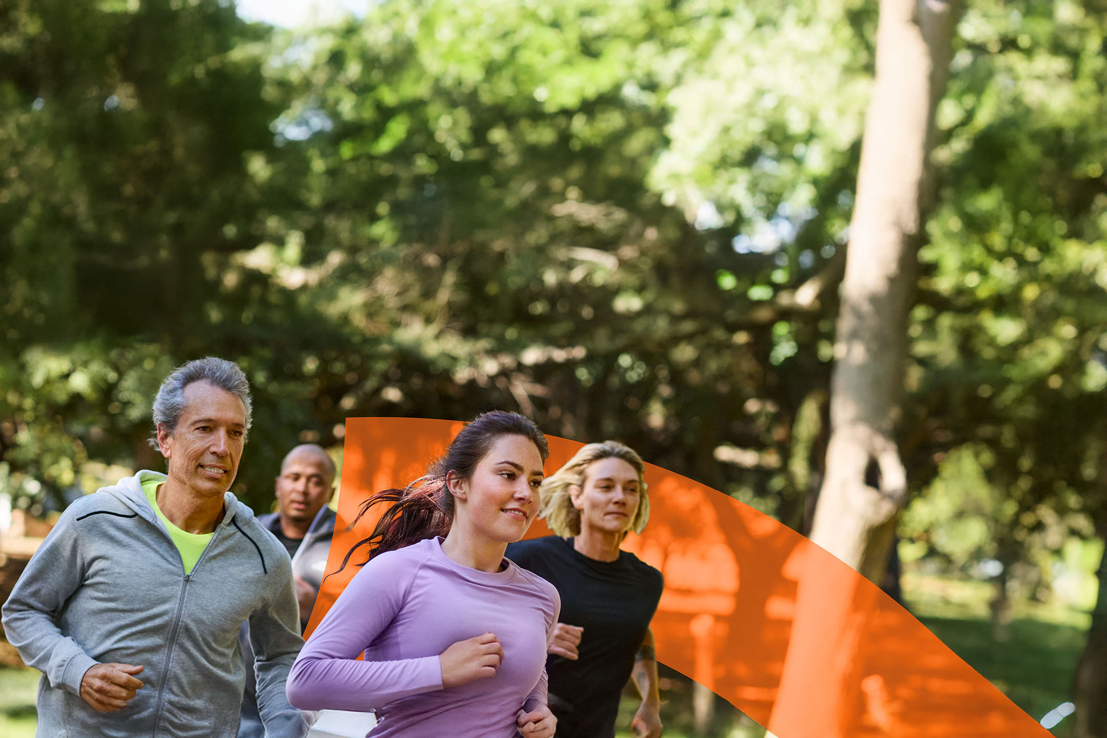 Quatre coureurs en tenue de sport courent en extérieur dans un parc.