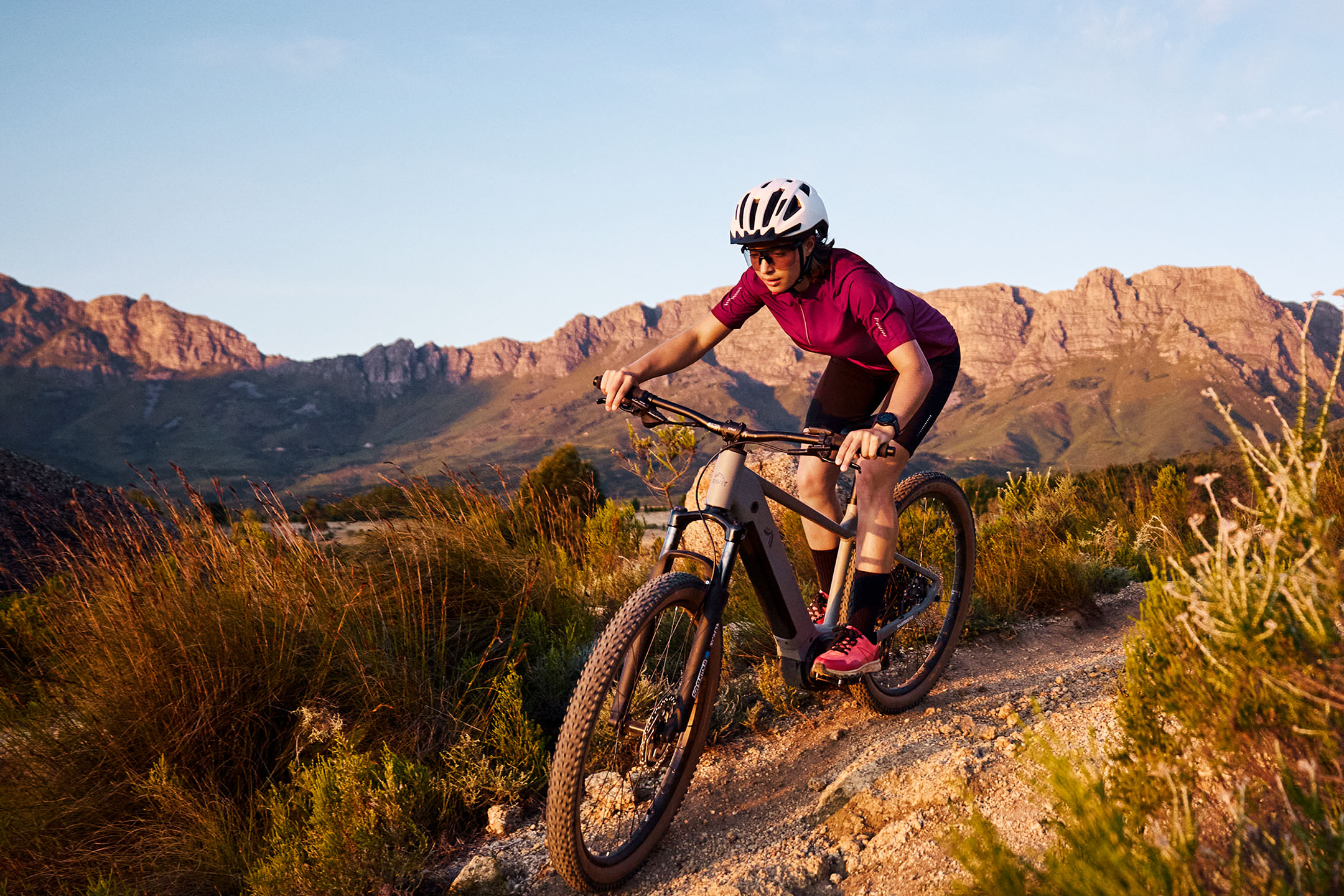 Femme faisant du VTT sur un sentier de terre avec des montagnes en arrière-plan.
