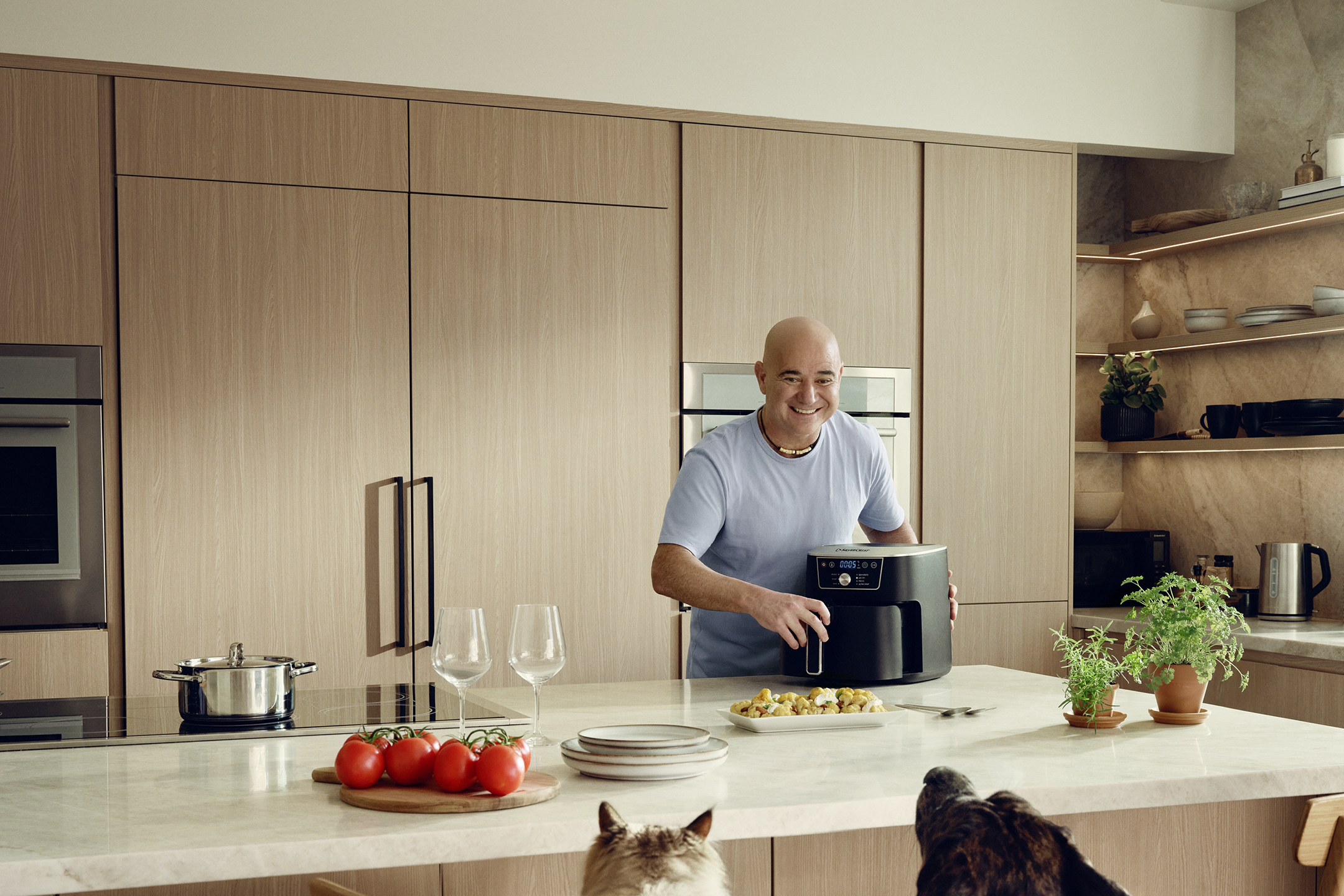 Andre Agassi dans la cuisine avec une friteuse à air chaud, des tomates et une casserole sur le plan de travail.