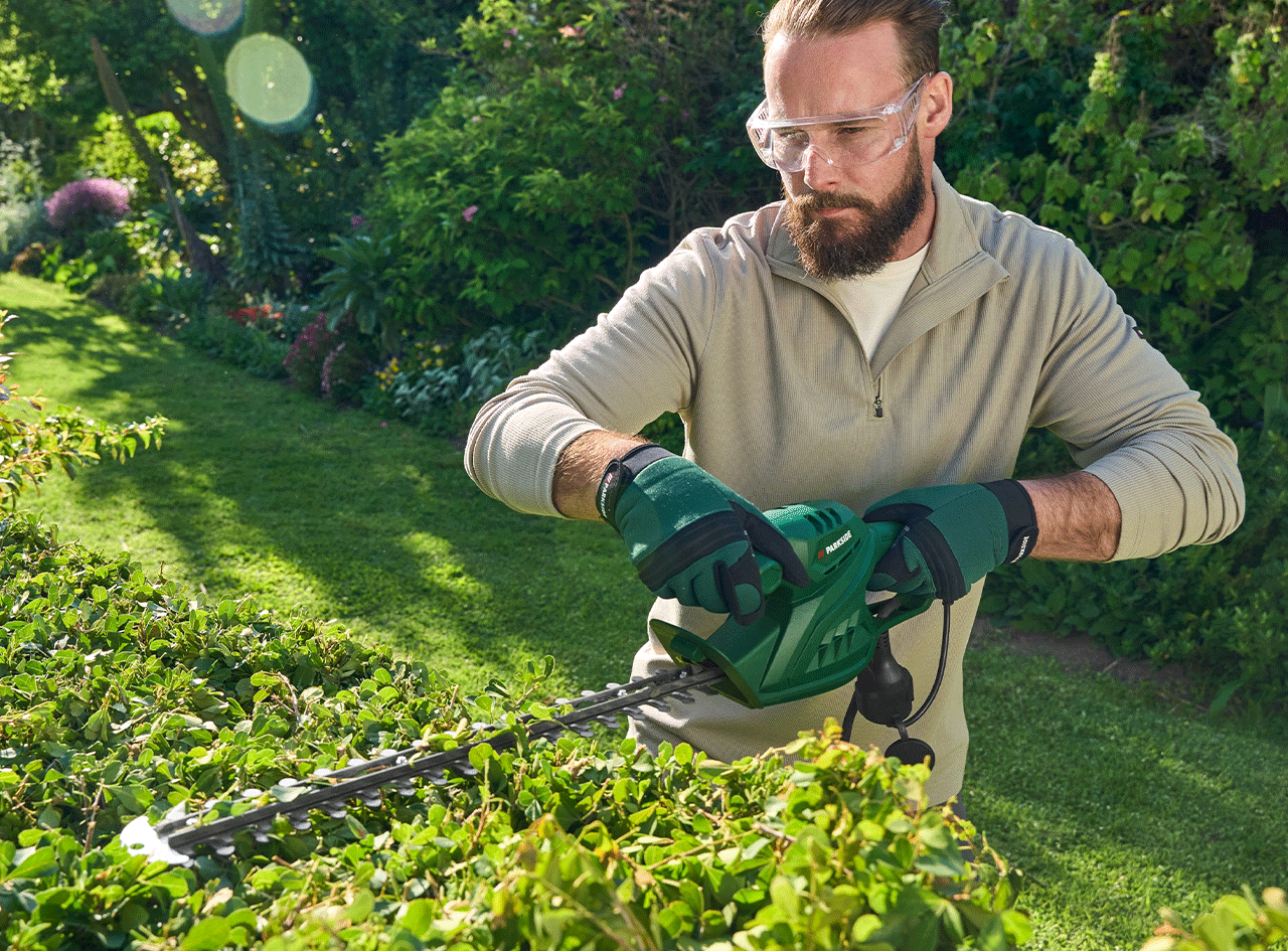 Un homme taille une haie avec un taille-haie électrique Parkside.